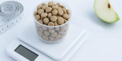 Measuring cup of diet dog kibble beside a dog scale and healthy-weight dog on a white background